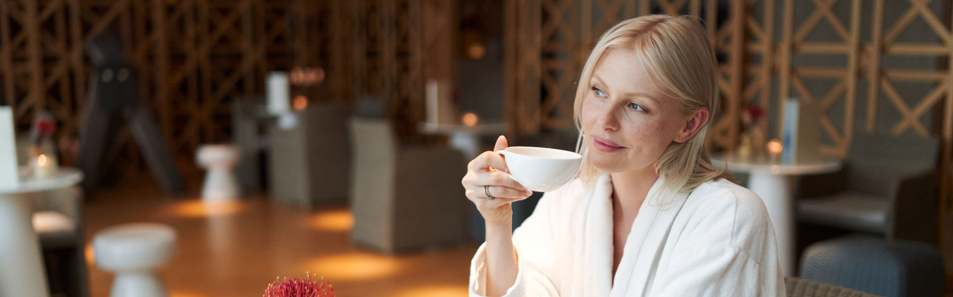 Eine Frau im Bademantel sitzt im Spa Café und Trinkt aus einer weißen Tasse