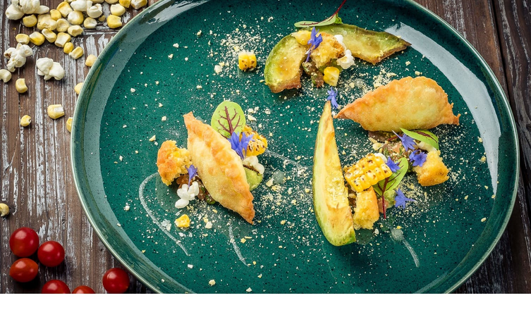 Restaurant dessert Gourmet plate with avocado, corn, edible flowers and fine dumplings on a green ceramic plate.