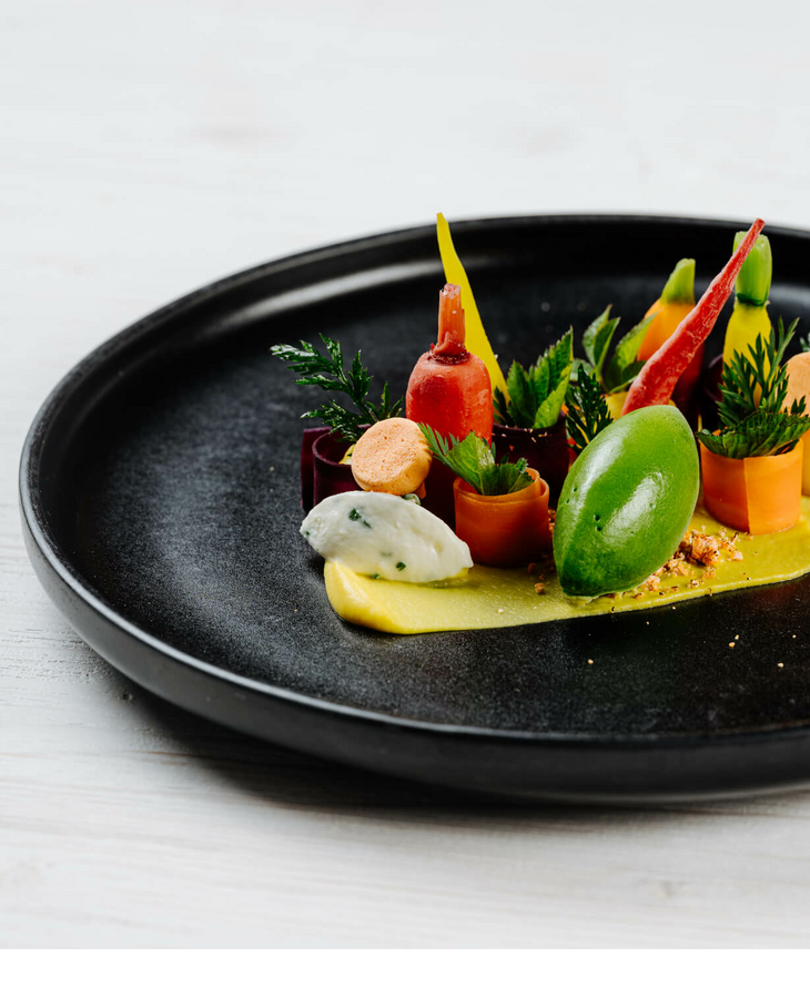 Dish at Tipken`s by Nils Henkel on Sylt An artfully prepared gourmet dish with colorful vegetables on a black plate.
