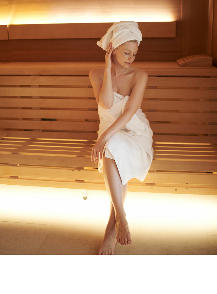 Eine Frau einem Handtuch bekleidet sitzt auf einer Holzbank in einer Sauna