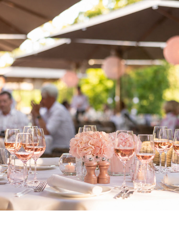 Wine glasses filled with rosé sit on a white tablecloth, flanked by candles and hydrangeas as decoration.