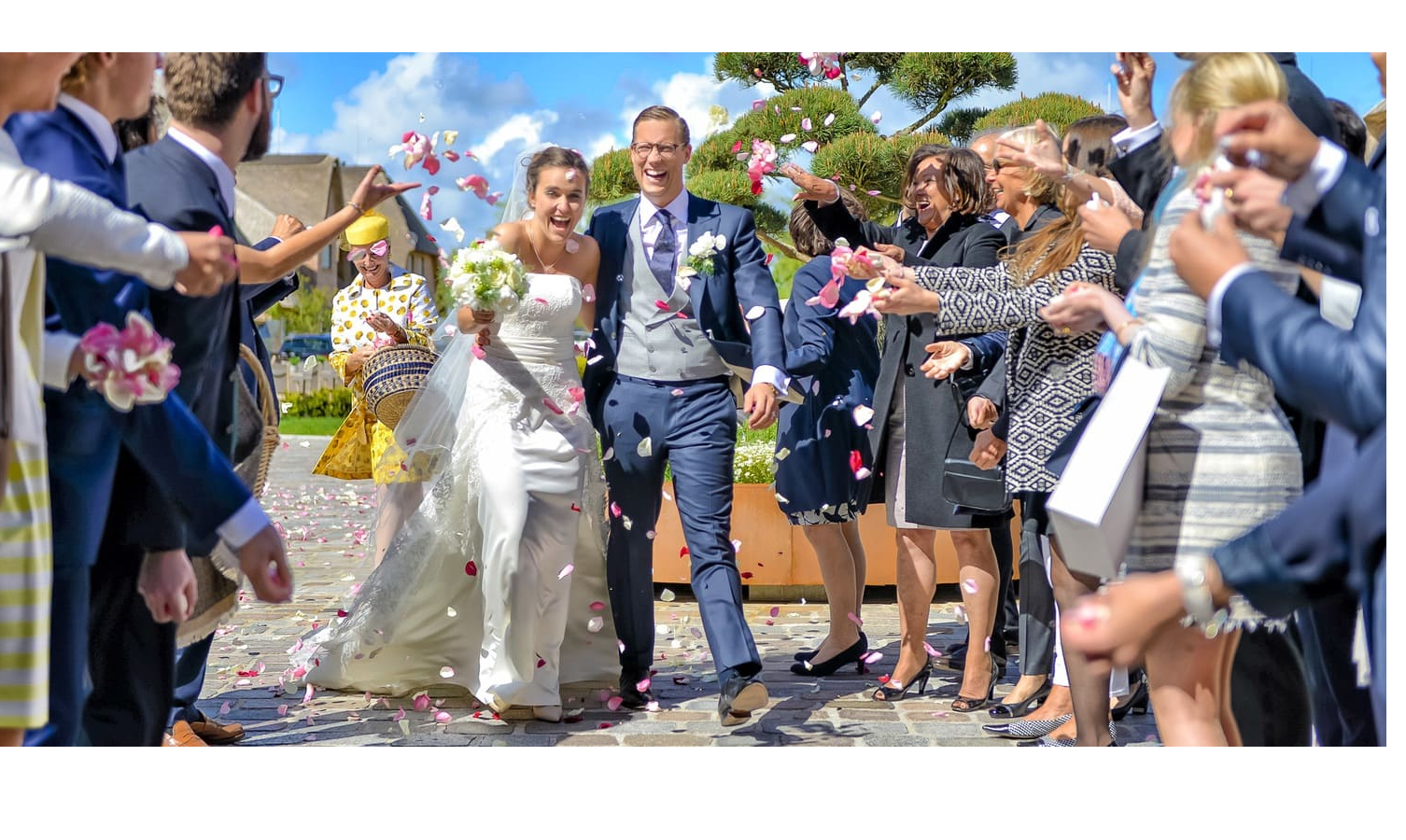 Begrüßung des Hochzeitspaares vor dem Hotel Severin*s auf Sylt Wedding couple under a blue sky, guests throwing petals, festive atmosphere at Severin*s Resort & Spa on Sylt.