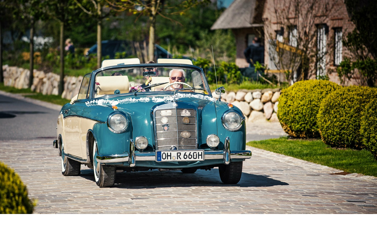 Mercedes Oldtimer biegt auf des Gelände das Hotel Severin*s ab Classic convertible on cobblestones in front of a hotel, surrounded by green countryside.