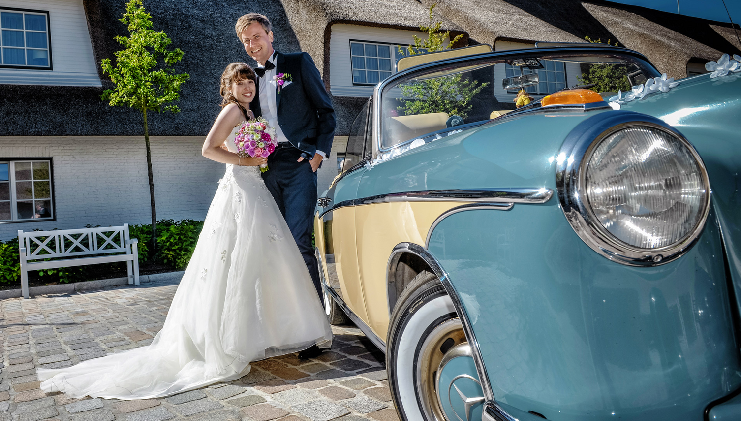 Brautpaar vor Mercedes Oldtimer und Gebäude des Hotel Severin*s auf Sylt Bride and groom in front of a vintage car at Severin*s Resort & Spa on Sylt, bright sunshine.